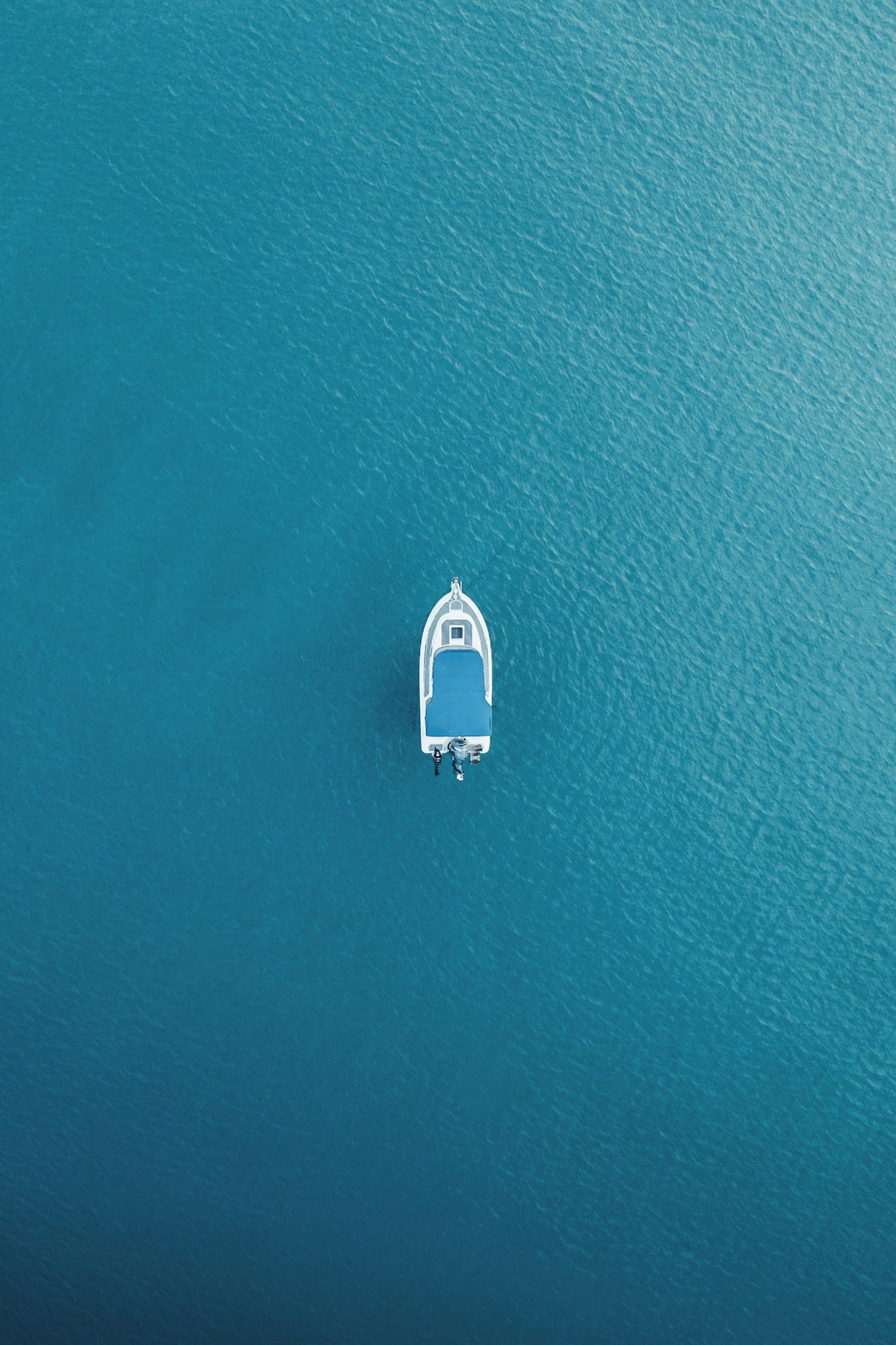 A single small boat seen from above, alone on deep navy sea.